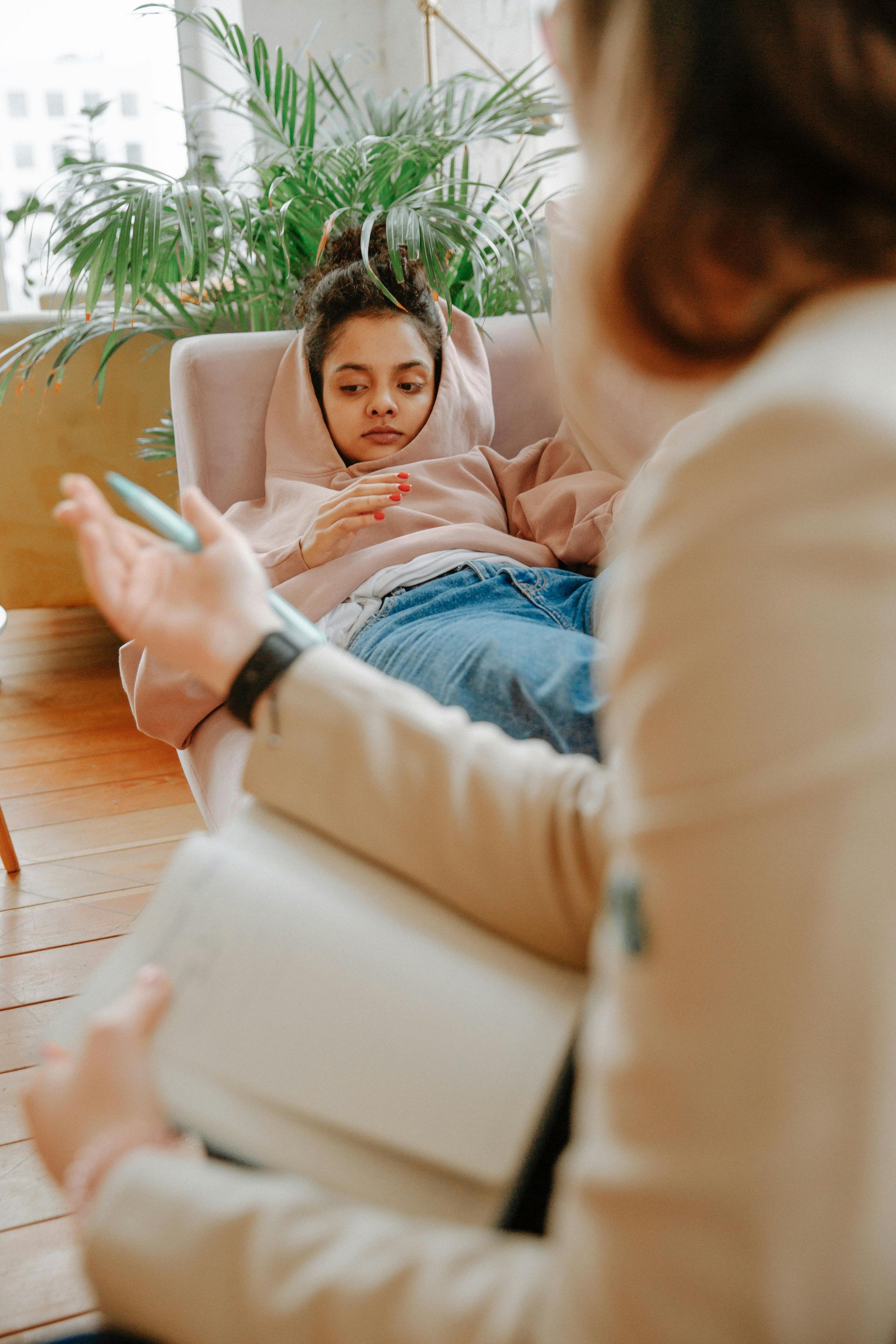 Therapist speaking with a child resting on a couch in a bright living room, with a notebook in hand