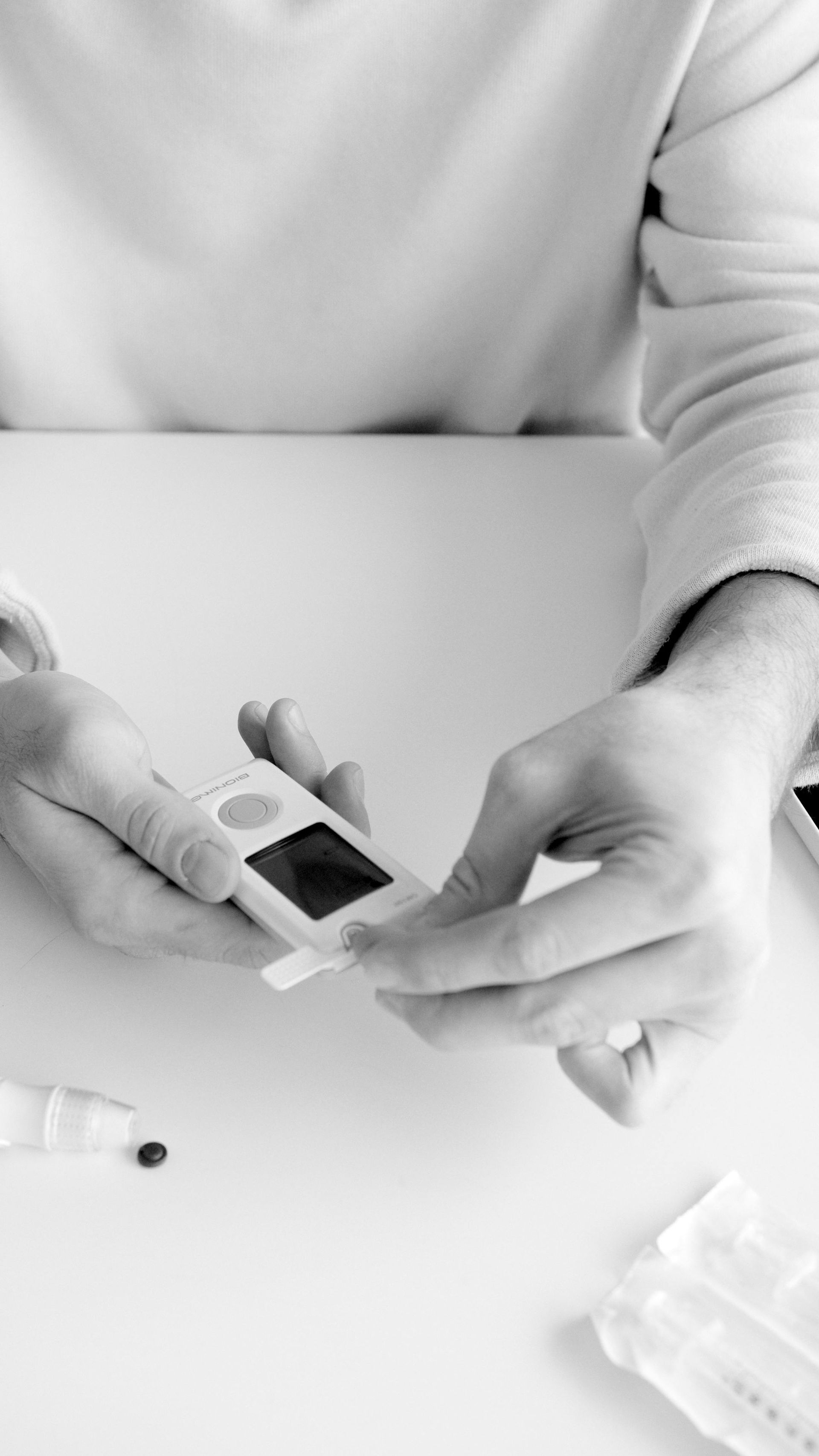 Hands checking blood sugar using a glucose meter and a test strip on a white surface.