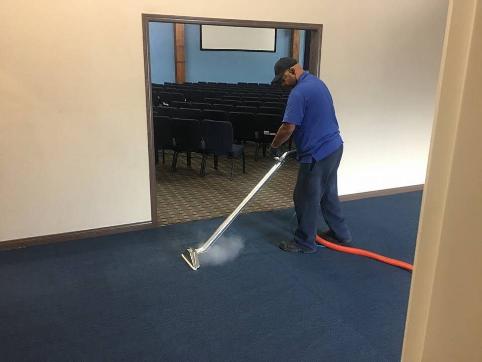 A woman is cleaning a carpet with a steam cleaner.