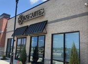 The exterior of a tan brick commercial building with black awnings, glass storefronts, and a sign reading