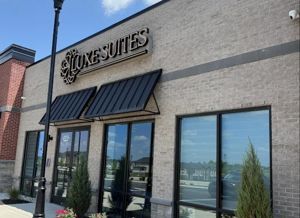 The exterior of a tan brick commercial building with black awnings, glass storefronts, and a sign reading 
