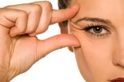 A hand pulls at the skin near an eye, demonstrating skin elasticity and the presence of fine lines.
