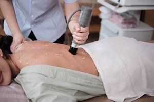 A practitioner uses an ultrasound therapy device with gel on a patient's back during a clinical treatment.
