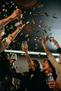 A group of people cheers with glasses raised as gold confetti falls in a dimly lit setting.
