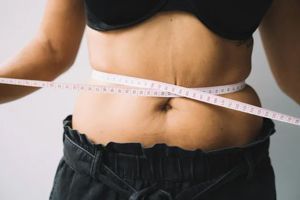 A torso midsection wrapped with a white measuring tape against a plain background.