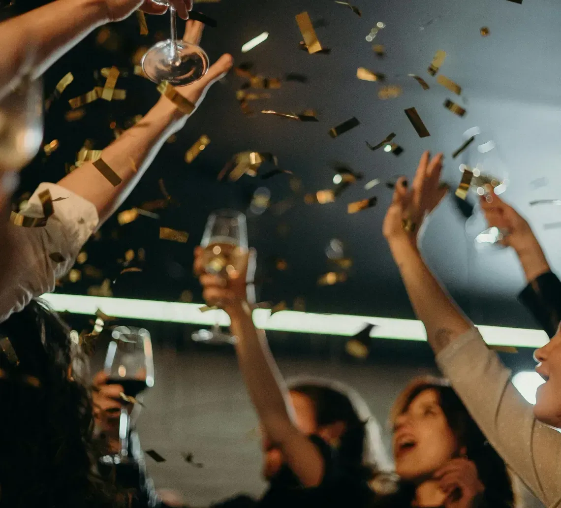 People holding glasses raised in celebration as golden confetti falls indoors.