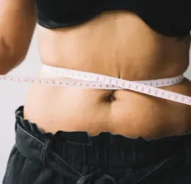 A torso measuring their waistline with a flexible white tape measure.