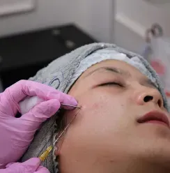 Gloved hands applying a facial treatment near a woman’s cheek in a clinic setting