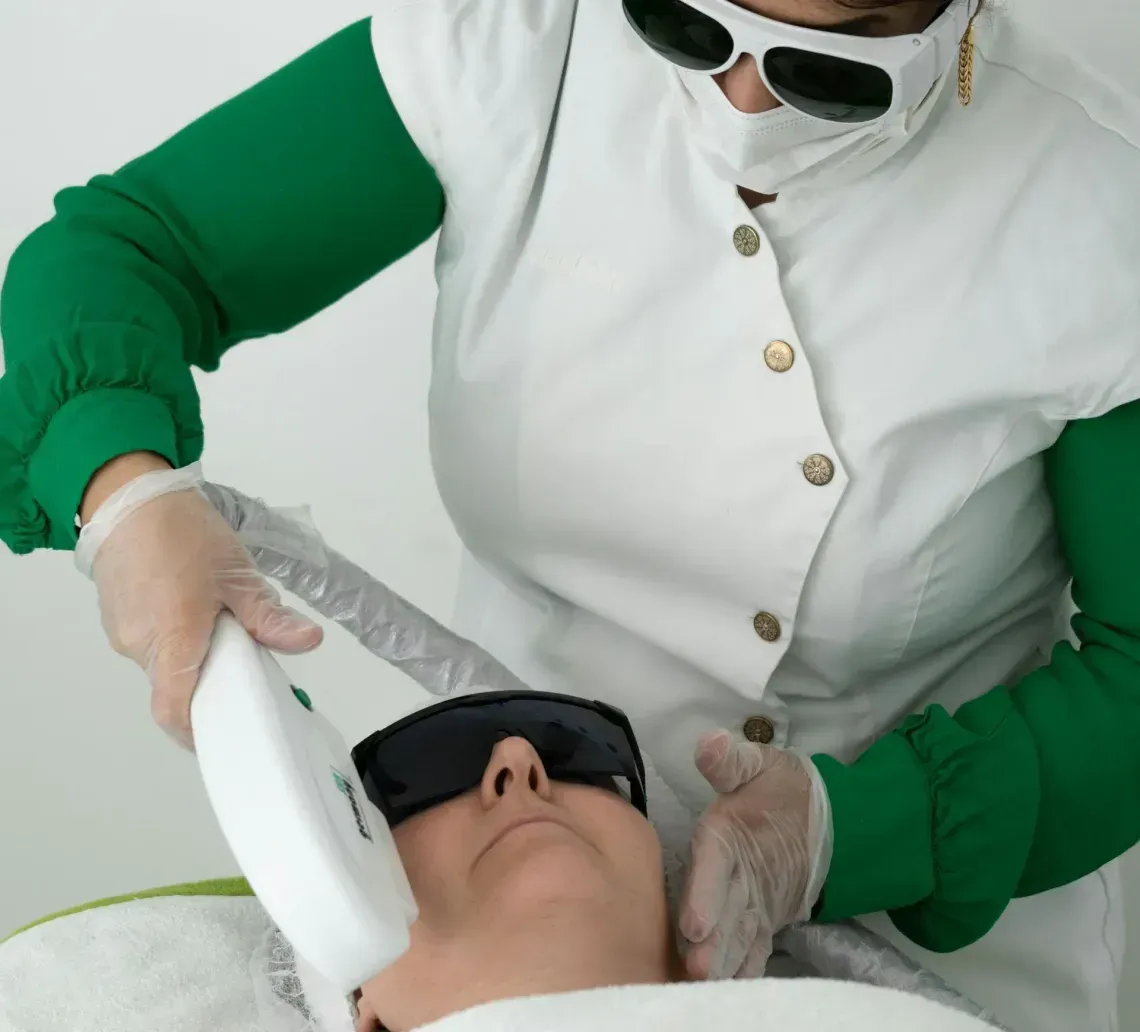 A professional performs a cosmetic laser treatment on a person wearing protective eyewear in a clinical setting.