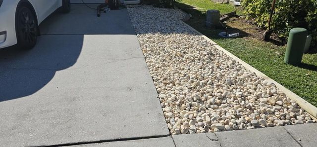 A white car is parked in a driveway next to a gravel path.