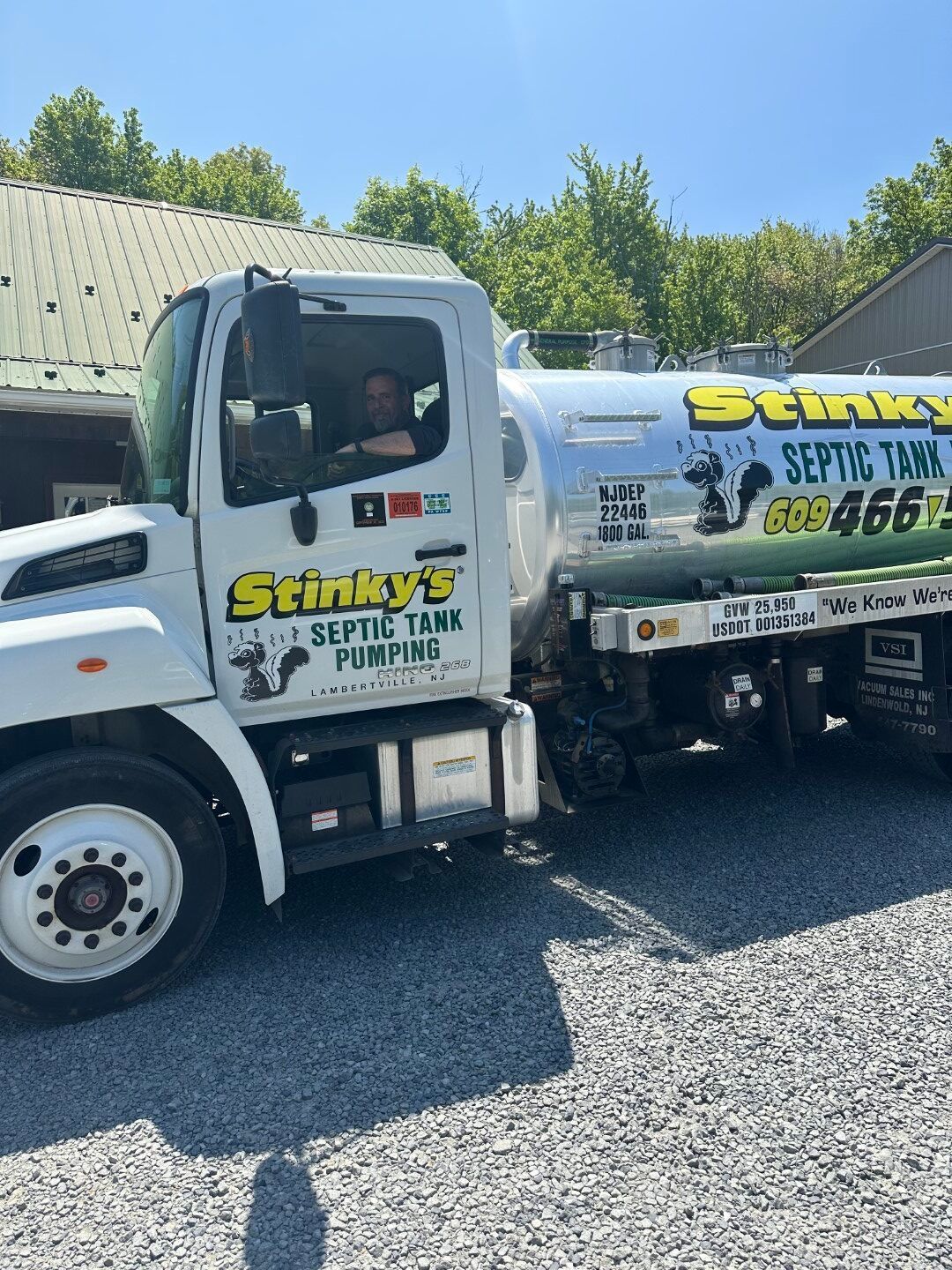 Two septic tank pumping trucks are parked next to each other in a gravel lot.
