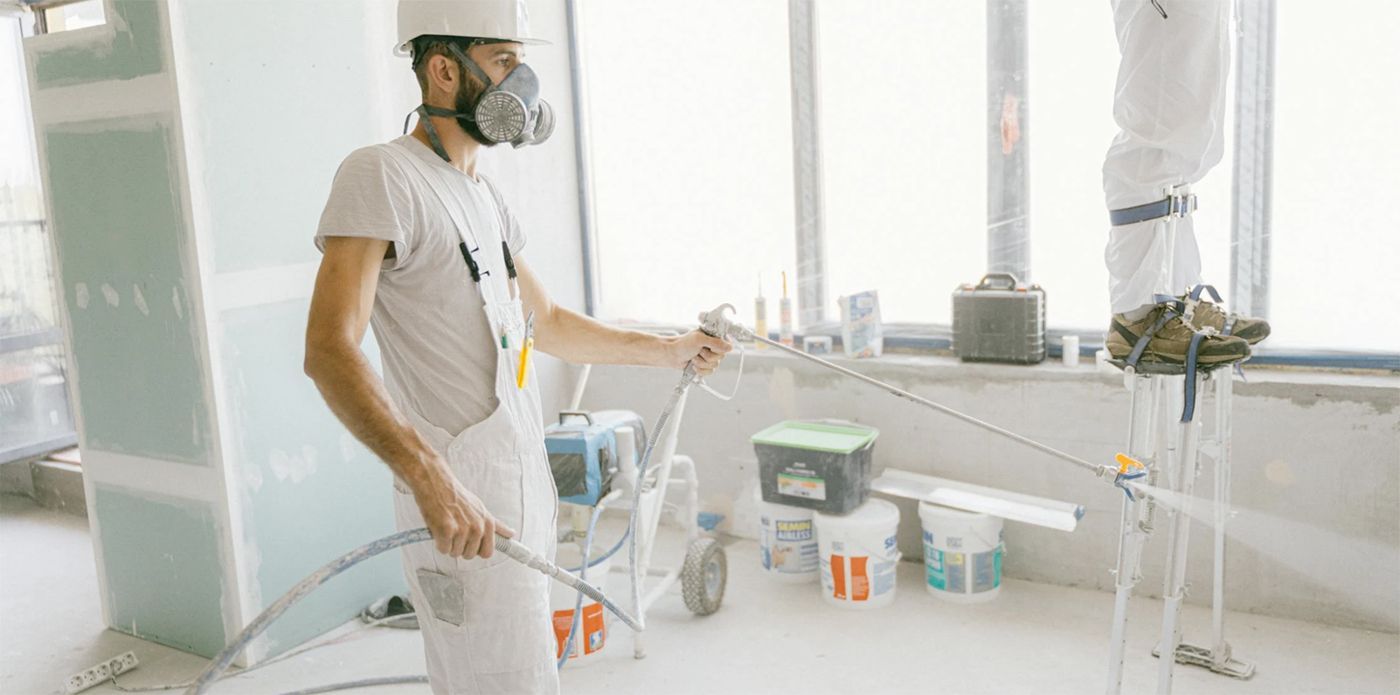 A man wearing a helmet and a mask is painting a room.