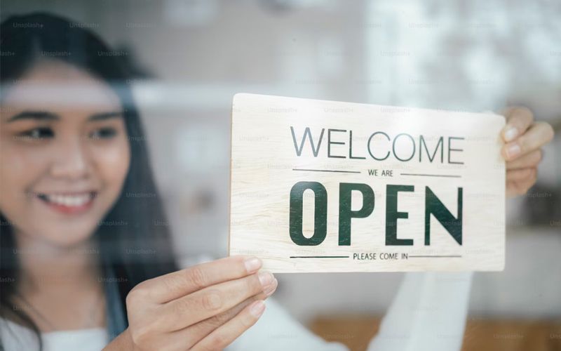 a woman is holding a welcome open sign in front of a window .