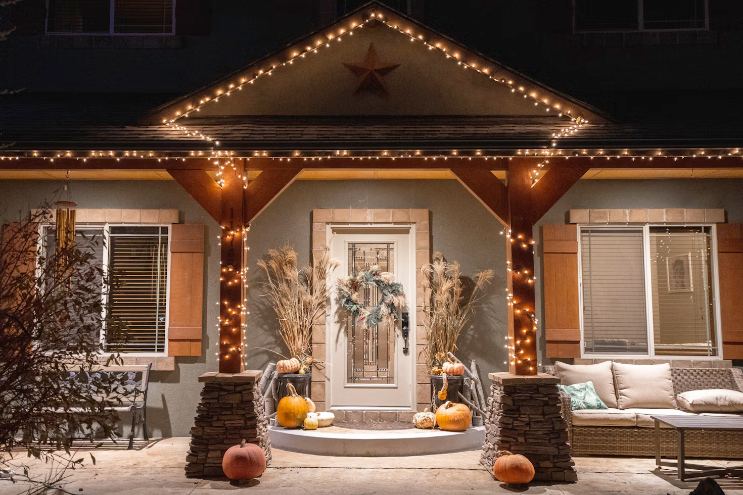 The front porch of a house decorated for fall with pumpkins and lights.