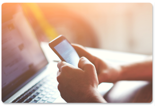 a person is typing on a laptop while holding a cell phone .