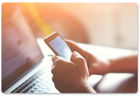 A person is holding a cell phone in front of a laptop.