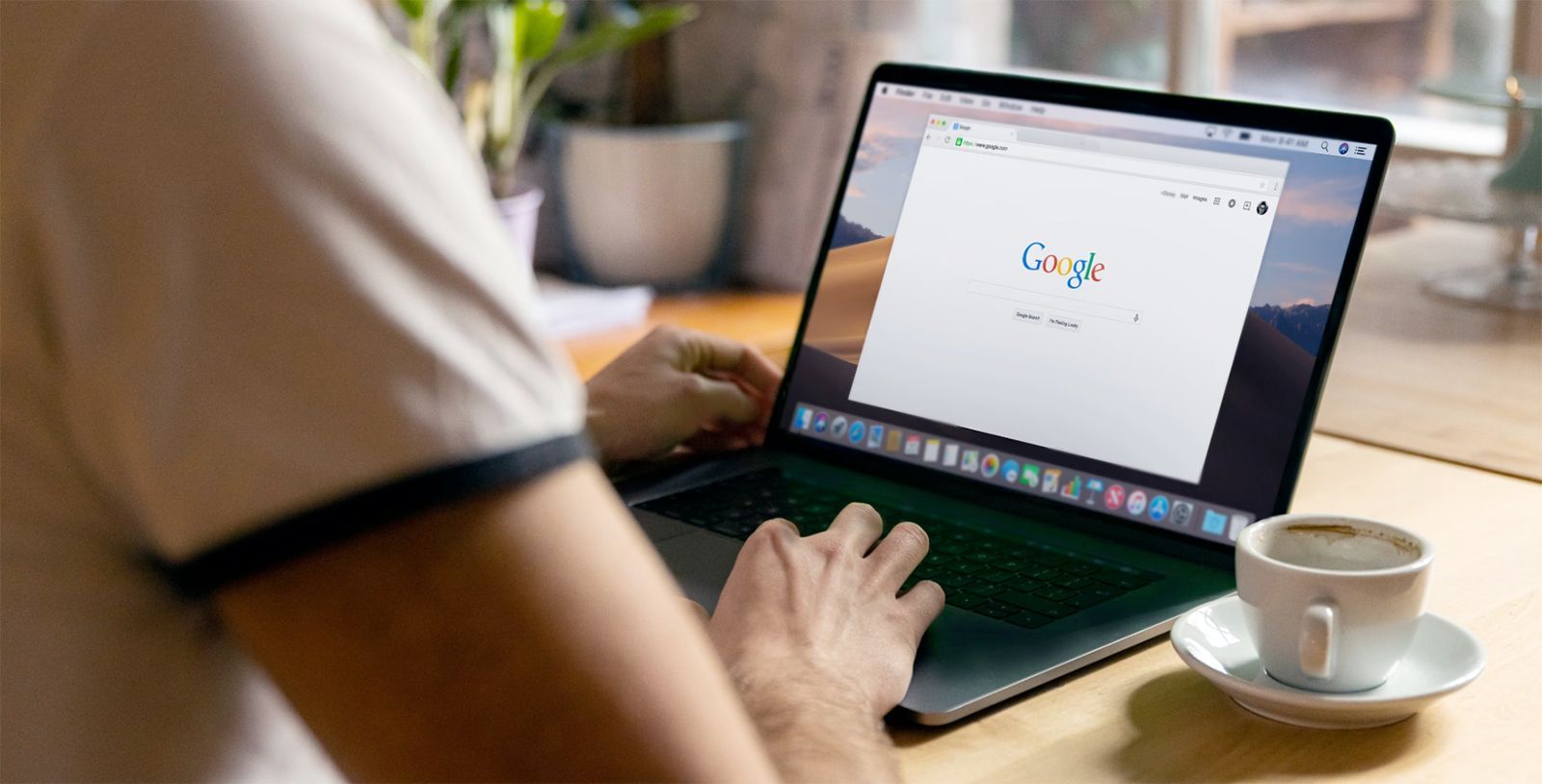 A person is typing on a laptop computer next to a cup of coffee.