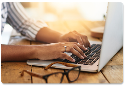 a woman is typing on a laptop computer while wearing glasses .