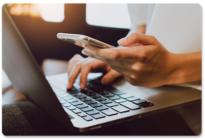 a man is sitting at a desk using a laptop and a cell phone .