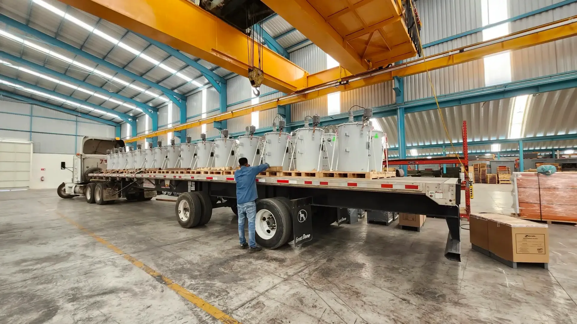 Worker beside flatbed trailer loaded with wrapped equipment inside a warehouse