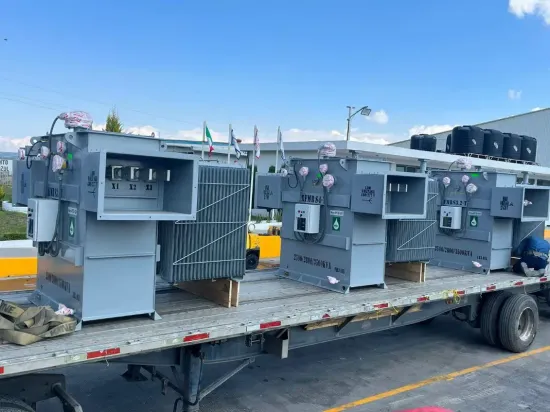 Gray industrial electrical equipment secured on a flatbed trailer outdoors under a blue sky