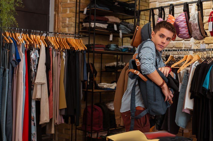 A young boy is holding a backpack in a clothing store.