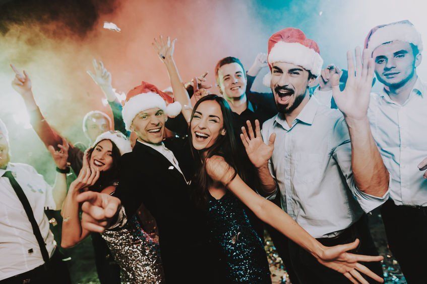 A group of people wearing santa hats are dancing at a christmas party.