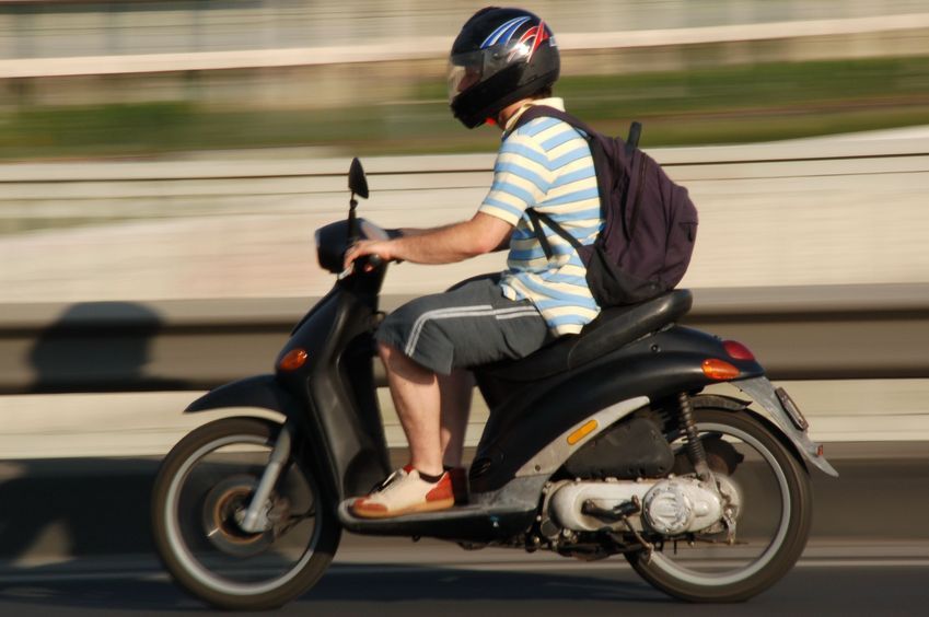 A man wearing a helmet is riding a scooter on a highway