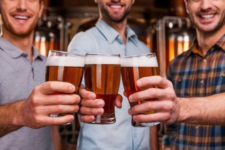 Three men are toasting with glasses of beer in a bar.