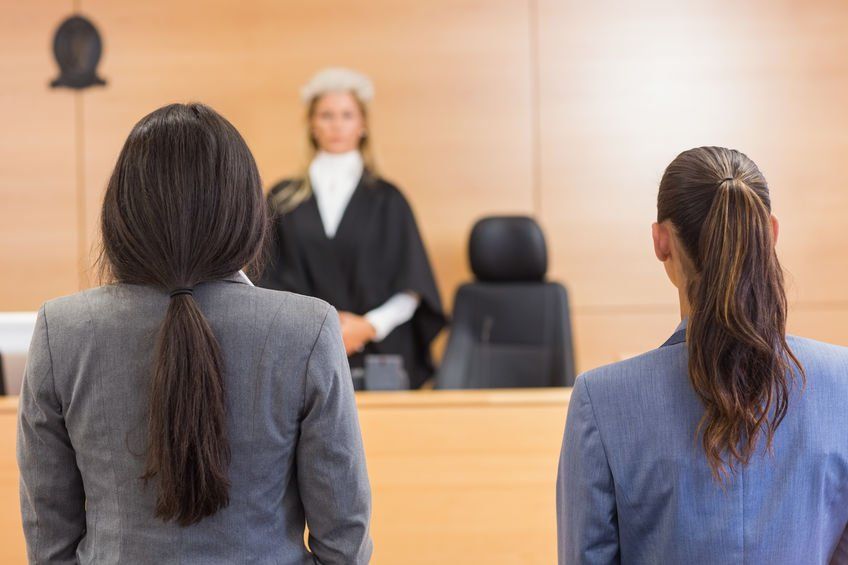 Two women are sitting in front of a judge in a courtroom.