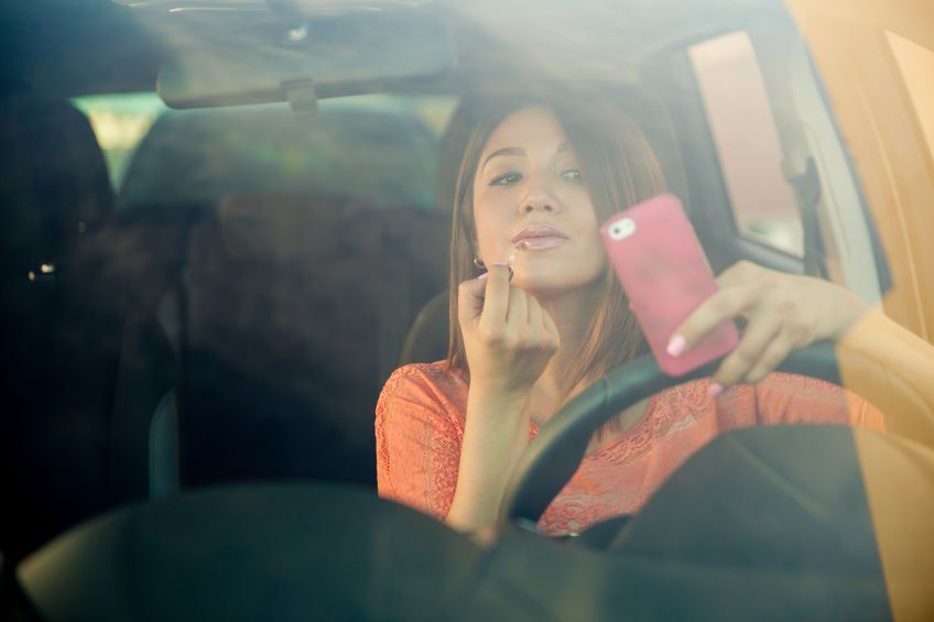 A woman is applying lipstick while driving a car.