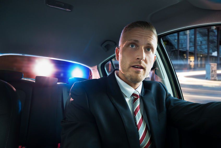 A man in a suit and tie is sitting in the back seat of a police car.
