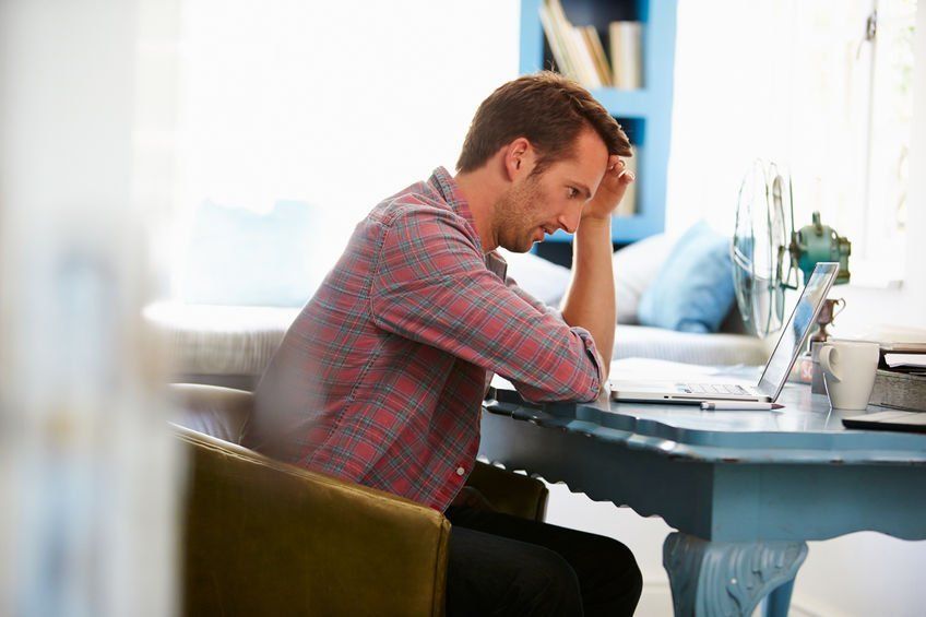 A man is sitting at a desk looking at a laptop computer.