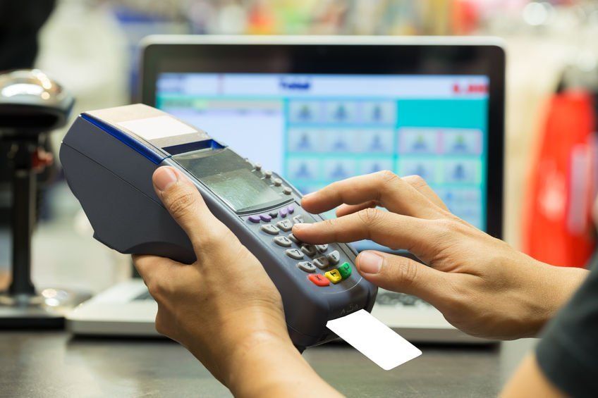 A person is using a credit card machine in front of a laptop.