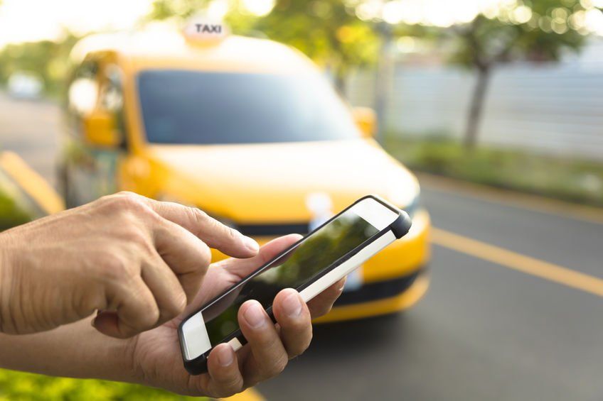 A person is using a cell phone in front of a taxi.