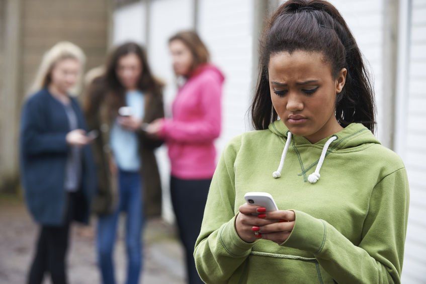 A girl is looking at her phone while a group of girls look at their phones.