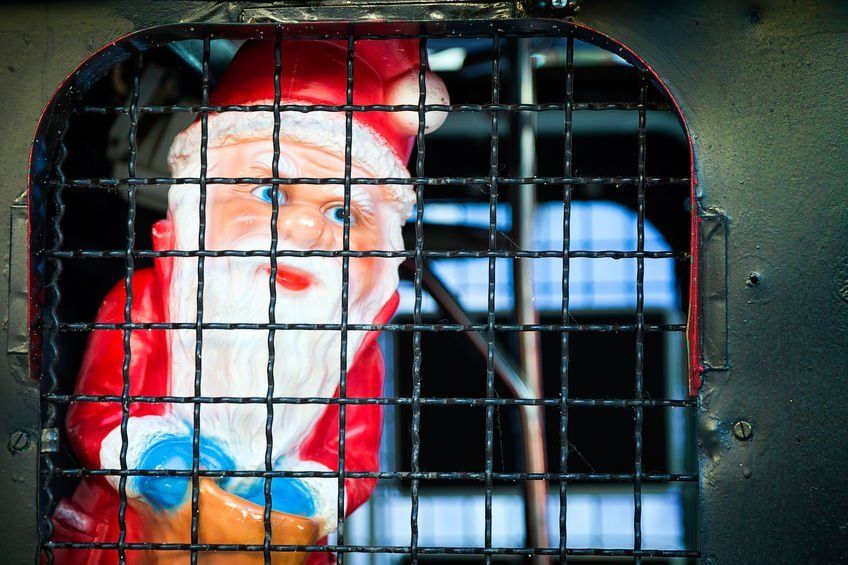 A santa claus figurine is behind bars in a cage.