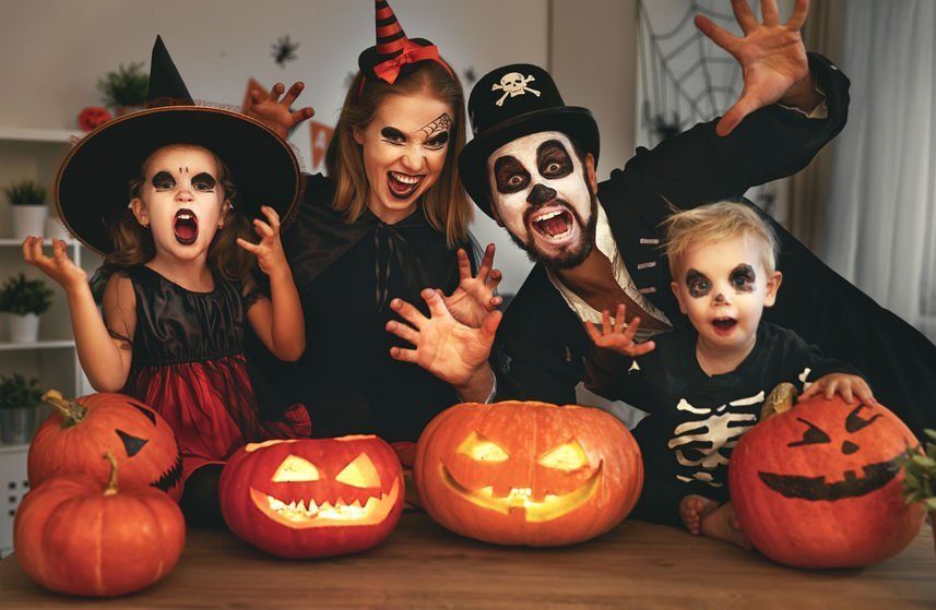 A family dressed in halloween costumes is sitting at a table with pumpkins.