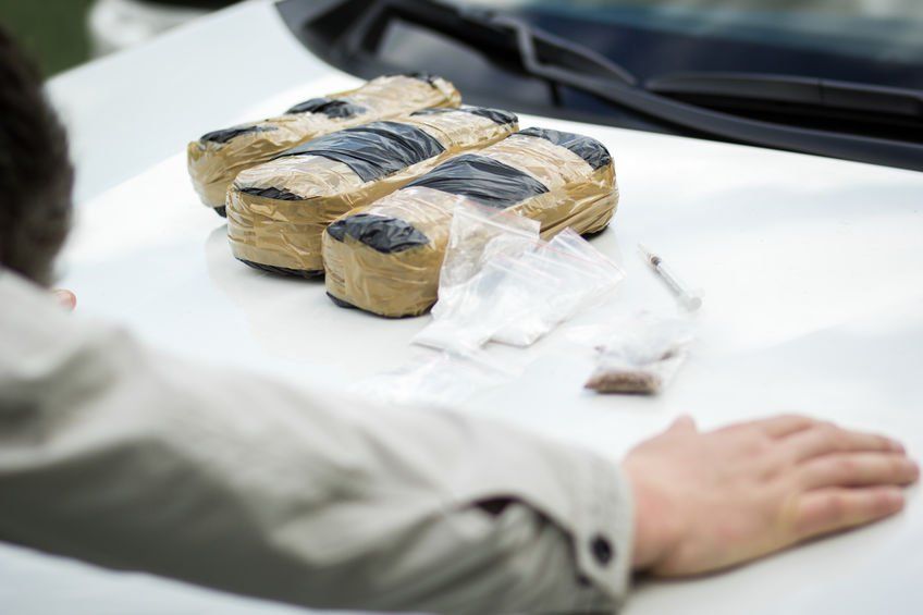 A man is looking at a pile of drugs on the hood of a car.