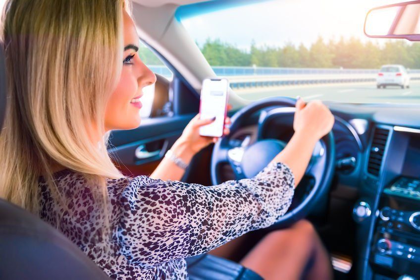 A woman is sitting in a car using a cell phone.