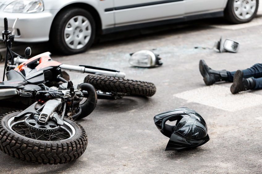 A person is laying on the ground next to a motorcycle and a car.