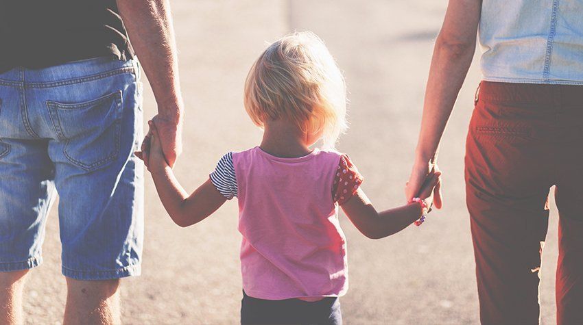 A little girl is holding hands with her parents while walking down the street.