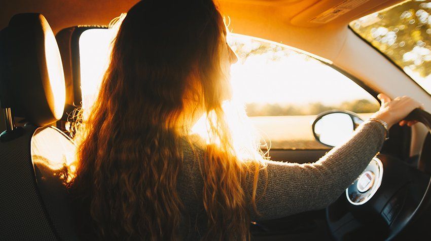 A woman is driving a car with the sun shining through the window.