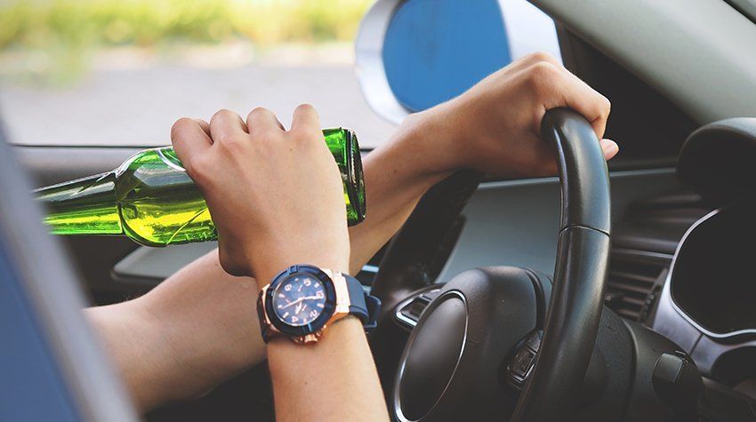 A person is holding a bottle of beer while driving a car.