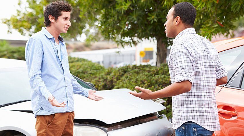 Two men are standing next to each other in front of a damaged car.