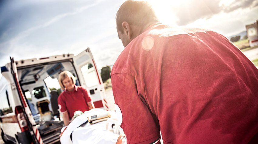 A man is carrying a stretcher in front of an ambulance.