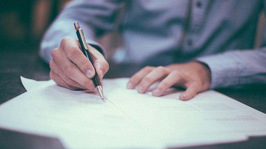 A man is writing on a piece of paper with a pen.