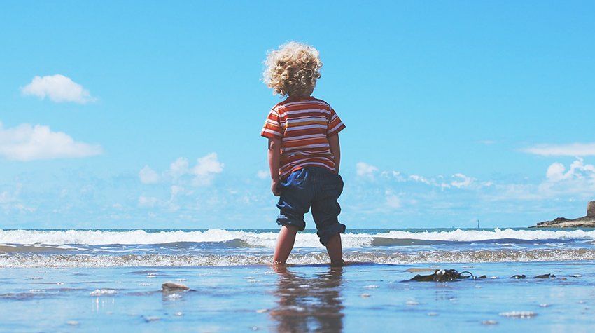 A young boy is standing on a beach looking at the ocean.