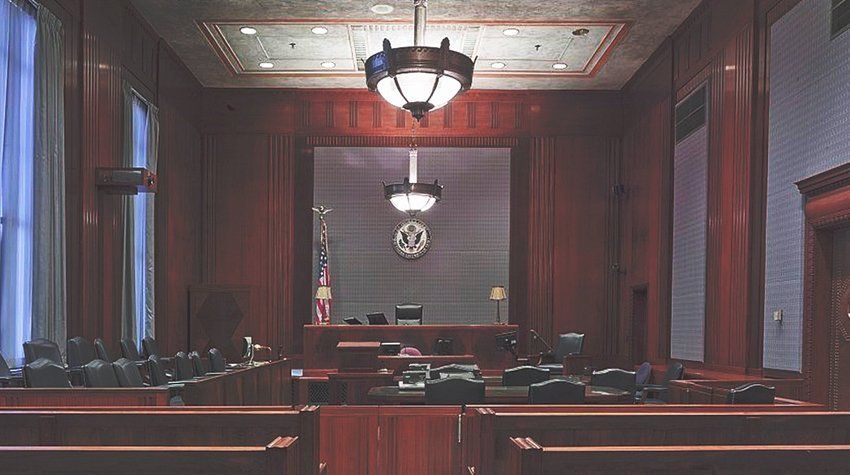 An empty courtroom with wooden benches and a chandelier hanging from the ceiling.