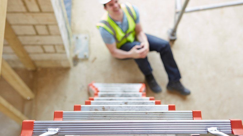 A construction worker is sitting on the floor next to a ladder.
